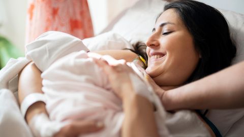 Eine Hebamme kümmert sich um eine Frau mit Neugeborenem auf einer Klinikstation