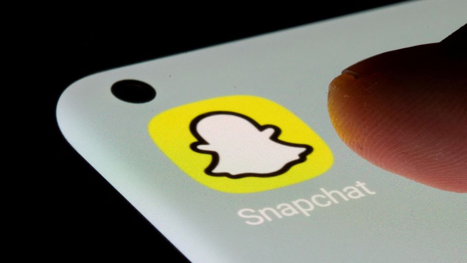 Das Logo der App Snapchat auf einem Handy-Bildschirm, darüber ein Daumen