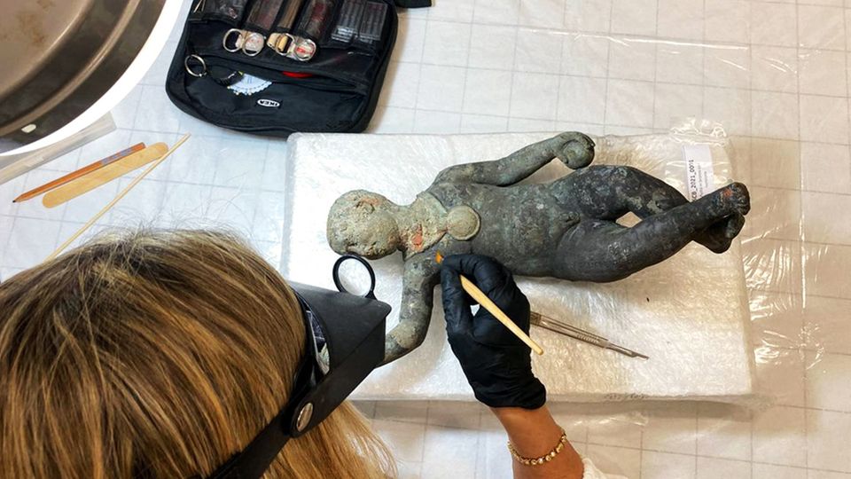 Forscherin untersucht Bronzefigur, die ein Kind darstelle