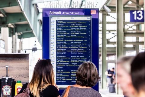 Menschen stehen vor einer Anzeigetafel mit Deutsche Bahn-Fahrplan