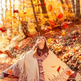 Eine Frau steht lachend unter herabfallendem Herbstlaub.