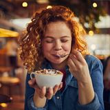 Eine junge Frau löffelt lächelnd ihren Kakao.