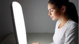 Eine Frau sitzt mit geschlossenen Augen vor einer Tageslichtlampe.