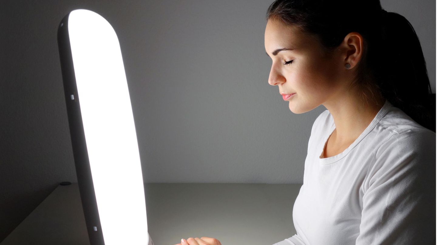 Eine Frau sitzt mit geschlossenen Augen vor einer Tageslichtlampe.