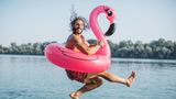 Ein Mann springt mit einer Flamingo-Luftmatratze in einen See.