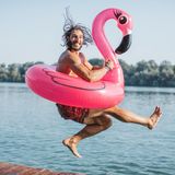 Ein Mann springt mit einer Flamingo-Luftmatratze in einen See.