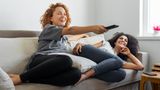 Zwei Frauen amüsieren sich auf dem Sofa gemeinsam.