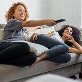 Zwei Frauen amüsieren sich auf dem Sofa gemeinsam.