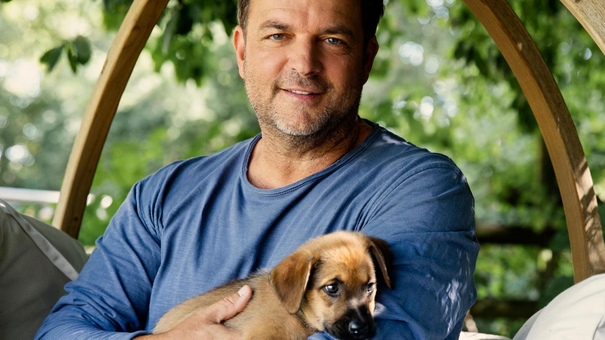 Hundetrainer Martin Rütter lächelt in einem Garten in die Kamera