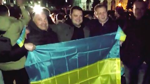 Drei Männer mit der Flagge der Ukraine in der Hand bejubeln in Cherson die Befreiung von den russischen Besatzern