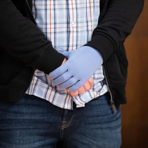 Ein weißer Mann in Karohemd, Jeans und Strickjacke steht in einem Gerichtssaal und umfasst mit einer Hand das andere Handgelenk