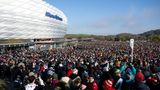 Vor der silbrig-weiß glänzenden Fassade der Allianz-Arena steht eine Menschenmenge