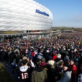Vor der silbrig-weiß glänzenden Fassade der Allianz-Arena steht eine Menschenmenge