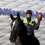 Ein Polizist auf einem schwarzen Pferd hält vor der Allianz-Arena mit links einen Football hoch