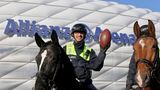 Ein Polizist auf einem schwarzen Pferd hält vor der Allianz-Arena mit links einen Football hoch