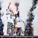 Ein junger Mann in Zebra-Hosen, weißem Football-Trikot, weißen Handschuhen und Maske steht auf einer Bühne in rappt in ein Mikro