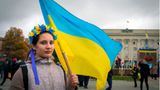 Eine junge Frau, die einen traditionellen Blumenkranz trägt, hält eine ukrainische Flagge.