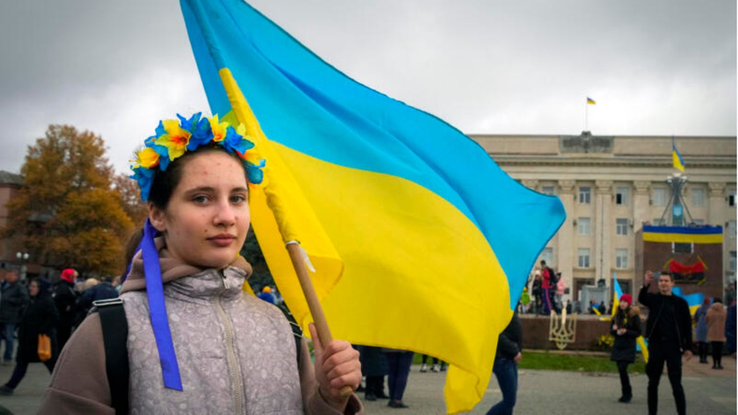 Eine junge Frau, die einen traditionellen Blumenkranz trägt, hält eine ukrainische Flagge.