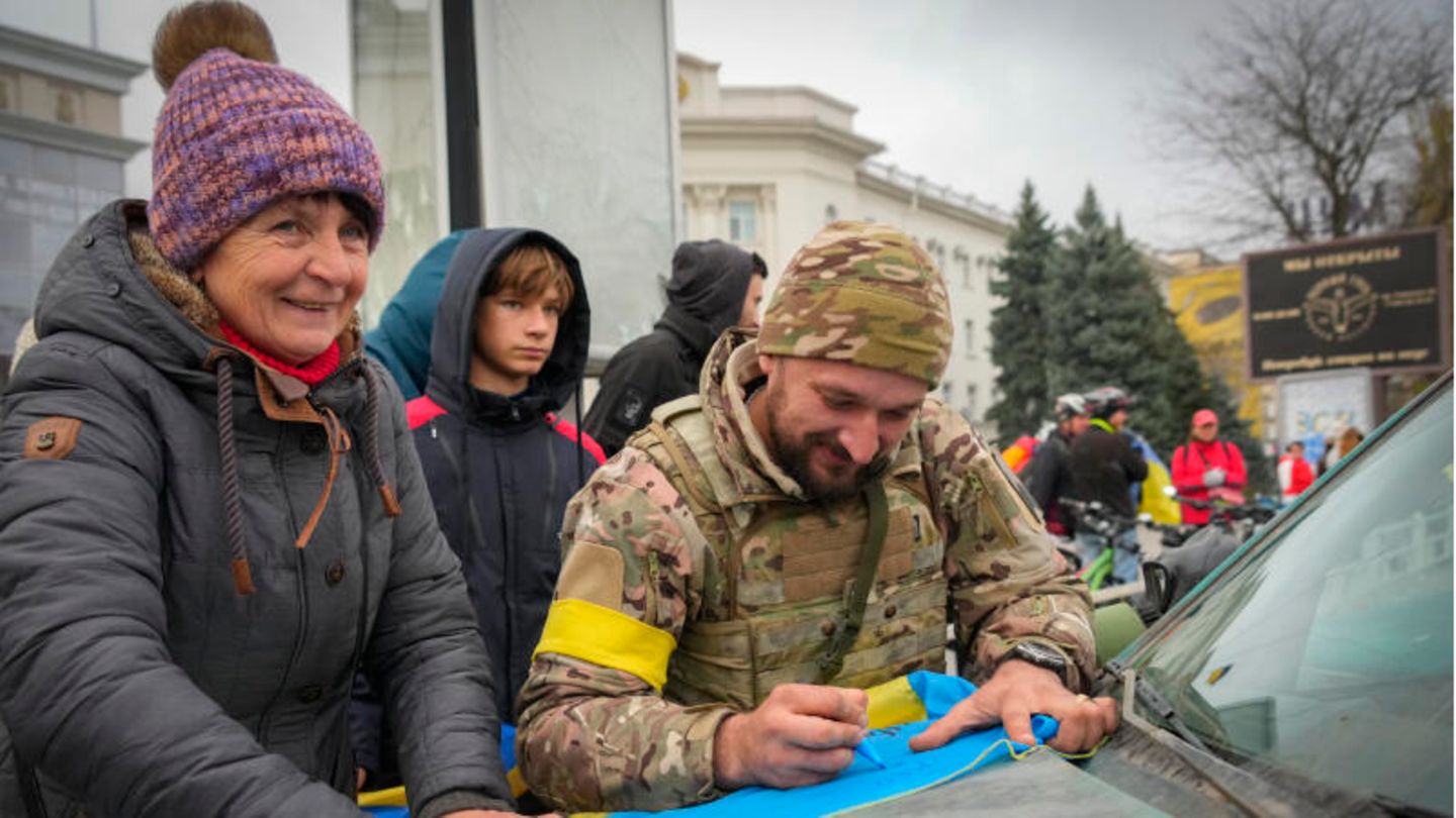 Ein ukrainischer Soldat schreibt auf eine Nationalflagge einer Anwohnerin