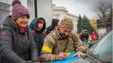 Ein ukrainischer Soldat schreibt auf eine Nationalflagge einer Anwohnerin