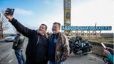 Motorradfahrer machen Selfies vor einem Straßenschild mit der Aufschrift "Cherson Oblast"