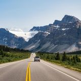 Ein Auto fährt auf einer weitläufigen Straße in Richtung Gebirge