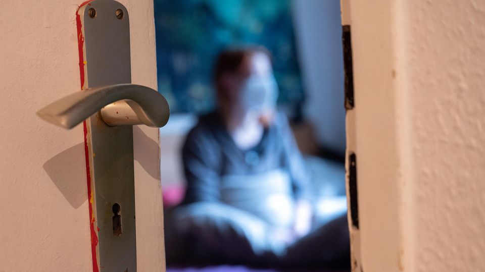 Blick durch Türspalt in ein Zimmer, in dem sich eine Corona-infizierte Frau isoliert hat