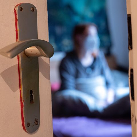 Blick durch Türspalt in ein Zimmer, in dem sich eine Corona-infizierte Frau isoliert hat