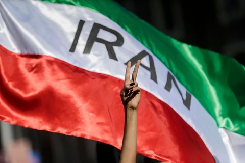 Eine Frau zeigt auf einer Demonstration für die Menschenrechte im Iran das Victory-Zeichen vor einer iranischen Fahne