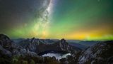 Über einem Bergsee strahlen Lichter in verschiedenen Farben am Nachthimmel