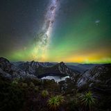 Über einem Bergsee strahlen Lichter in verschiedenen Farben am Nachthimmel