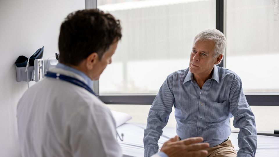 Ein Mann sitzt auf der Arztliege und spricht mit einem Doctor.