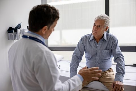 Ein Mann sitzt auf der Arztliege und spricht mit einem Doctor.