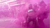 In einer rosafarbenen Rauchwolke entfernen Polizisten in Einsatzkleidung einen Demonstranten