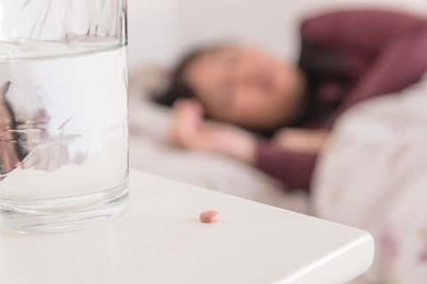 Frau im Bett mit Pille auf dem Nachtschrank