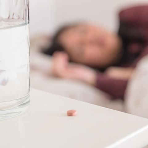 Frau im Bett mit Pille auf dem Nachtschrank