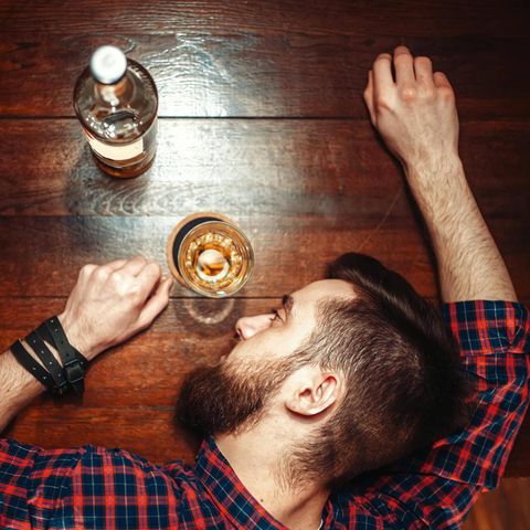 Ein Mann hat den Kopf neben einem Whiskyglas auf dem Tisch abgelegt