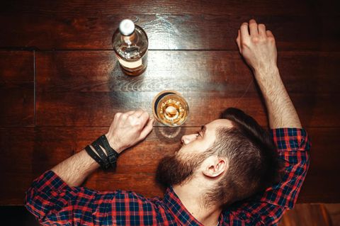 Ein Mann hat den Kopf neben einem Whiskyglas auf dem Tisch abgelegt