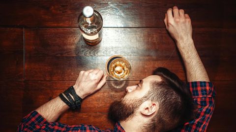 Ein Mann hat den Kopf neben einem Whiskyglas auf dem Tisch abgelegt