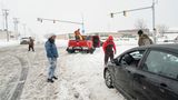 Mehrere Personen stehen auf einer eingeschneiten Straße. Ihr Auto ist offenbar im Schnee stecken geblieben.