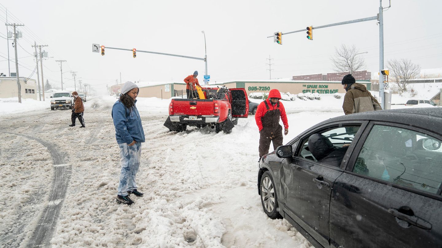 Mehrere Personen stehen auf einer eingeschneiten Straße. Ihr Auto ist offenbar im Schnee stecken geblieben.