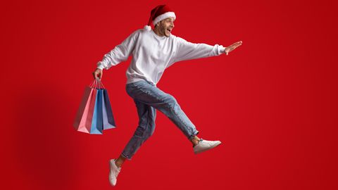 Black Friday Woche 2022: Ein Mann springt mit Einkaufstüten in der Hand vor Freude in die Luft.