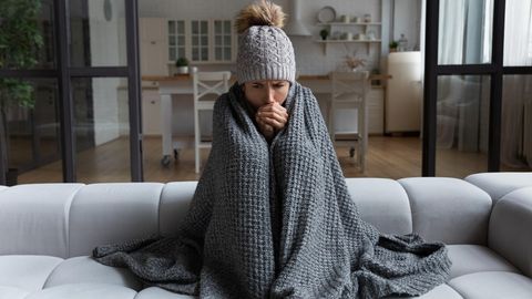 Kälte: Frau sitzt dick angezogen auf dem Sofa und friert
