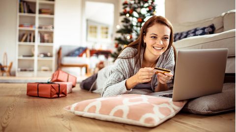 Apple Deals Black Week 2022: Frau liegt mit Laptop und Kreditkarte in weihnachtlicher. Wohnung auf dem Parkett