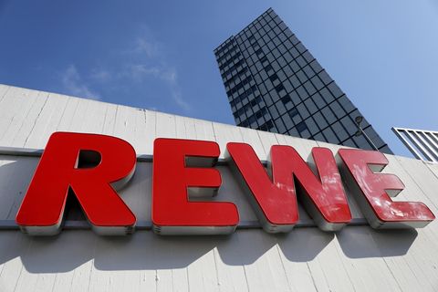 Ein Rewe Schriftzug hängt vor einem Supermarkt