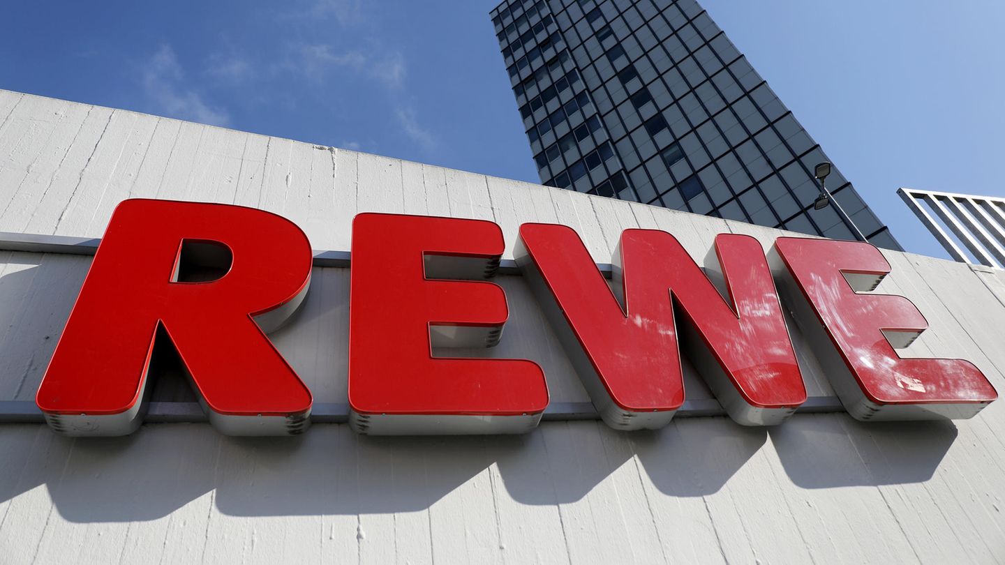 Ein Rewe Schriftzug hängt vor einem Supermarkt