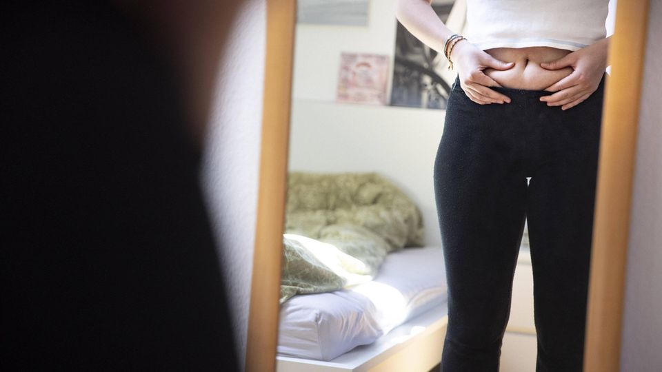 Heroin Chic Schönheitsideal Frau steht vor dem Spiegel und kneift sich in den Bauch