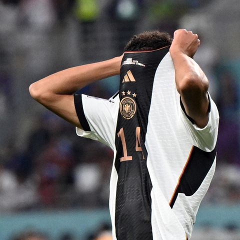 Ein Fußball-Profi im Deutschland-Trikot zieht sich mit beiden Händen den Kragen über das Gesicht