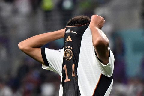 Ein Fußball-Profi im Deutschland-Trikot zieht sich mit beiden Händen den Kragen über das Gesicht