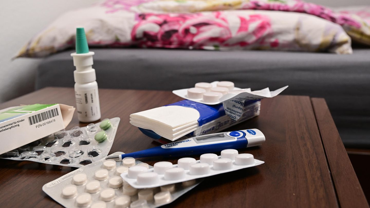 Verschiedene Medikamente, Nasenspray, ein Taschentuch und ein Fieberthermometer liegen auf einem Nachttisch